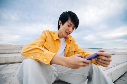 Young man in outdoor setting smiling while using smartphone