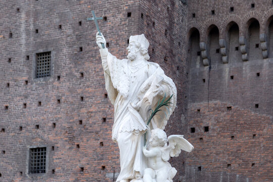 View of the statue of Saint John of Nepomuk with a small angel figure in front of the historic brick walls of Sforzesco Castle in Milano, Lombardia, Italy.