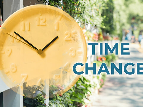 Yellow analog wall clock outdoors with Time Change text overlay for daylight savings concept