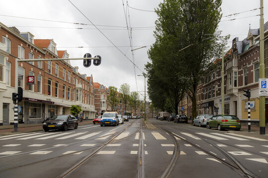 View of a street with tram tracks, historic brick buildings, parked cars, and trees under an overcast sky in Den Haag, Zuid-Holland, Netherlands.
