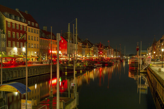 View of the colorful historic buildings and illuminated restaurants along the Nyhavn canal at night in Copenhagen, Denmark.