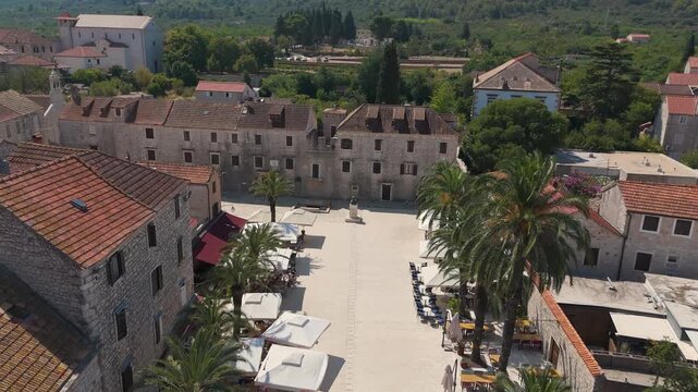 Historic Stari Grad square is framed by old houses, outdoor cafes, and tall palms on a bright summer day.