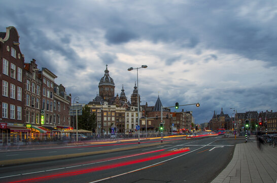 View of the Basilica of Saint Nicholas illuminated at dusk with long exposure light trails from traffic on the street in Amsterdam, North Holland, Netherlands.