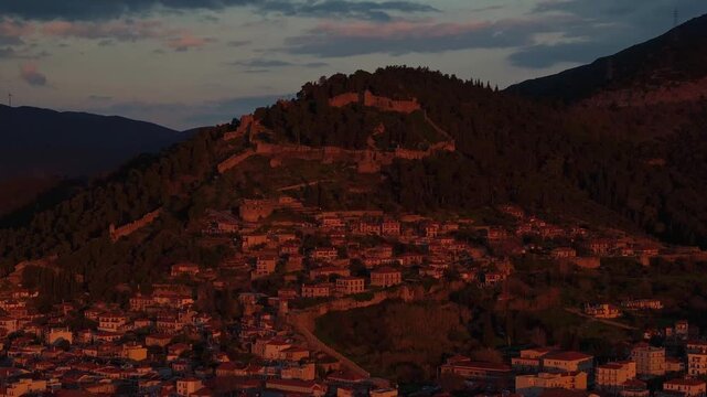 Close-up drone aerial shot of the historic Nafpaktos castle and Venetian fortress walls on the hill, glowing in intense red and golden sunrise light against a dramatic morning sky in Greece.