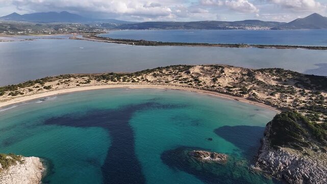 High-altitude drone orbiting shot revealing the iconic Omega shape of Voidokilia Beach, its turquoise waters, sand dunes, and the adjacent Gialova Lagoon in Messenia, Peloponnese, Greece.