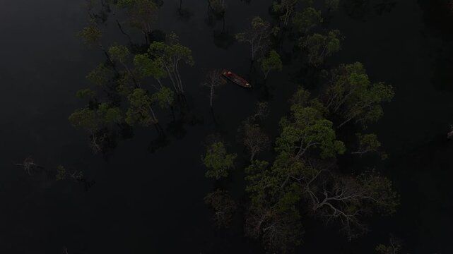 Aerial drone view of a fisherman rowing across Tuyen Lam Lake at sunrise near Suoi Tia in Xuan Huong, Da Lat, Vietnam, surrounded by peaceful pine forests.