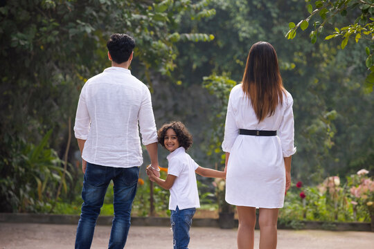 Back view of Indian parents with their son holding hands and walking in park