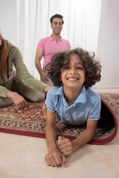 Child boy lying down on carpet and looking at camera while his parents sitting behind