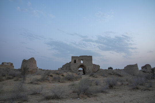 View of the ancient ruins of Bijnot Fort with weathered stone walls and an arched gateway set against a desert landscape in Bijnot, Punjab, Pakistan.