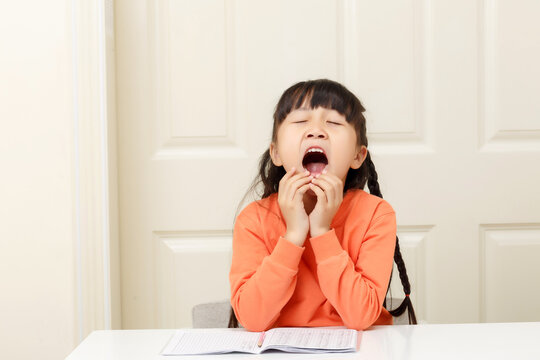 Sleepy little girl yawning with her mouth wide open during a home study session.