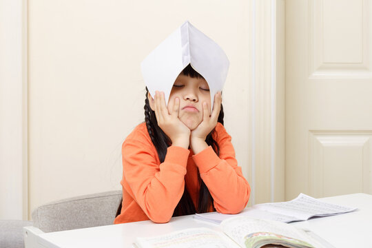 Exhausted young student resting her head with a book over her forehead in frustration.