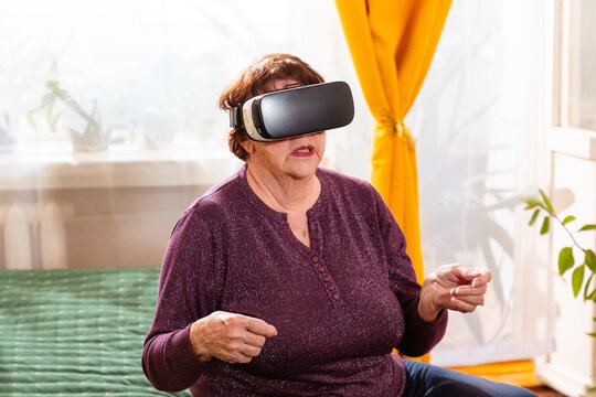 Mature Caucasian woman enjoys interactive virtual reality while sitting on a cozy sofa. Modern home recreation and digital lifestyle for older generations. Mid shot