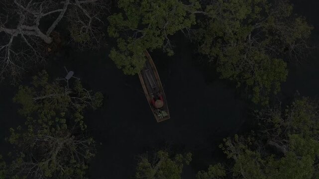 Aerial drone view of a fisherman rowing across Tuyen Lam Lake at sunrise near Suoi Tia in Xuan Huong, Da Lat, Vietnam, surrounded by peaceful pine forests.