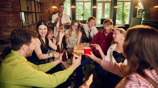 Office coworkers sharing pizza and red cups during friendly team gathering. Concept of food service websites, employee event pages and corporate culture content.