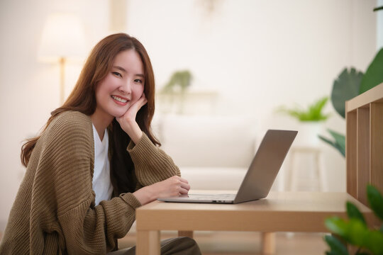 Smiling Asian woman studying with a laptop at home, representing online learning, distance education, university study, digital technology