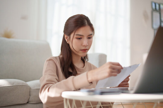 Asian woman reviewing household bills and financial documents, managing monthly expenses, personal budget, payments, debt, income and everyday financial planning.