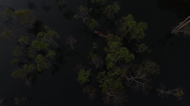 Aerial drone view of a fisherman rowing across Tuyen Lam Lake at sunrise near Suoi Tia in Xuan Huong, Da Lat, Vietnam, surrounded by peaceful pine forests.