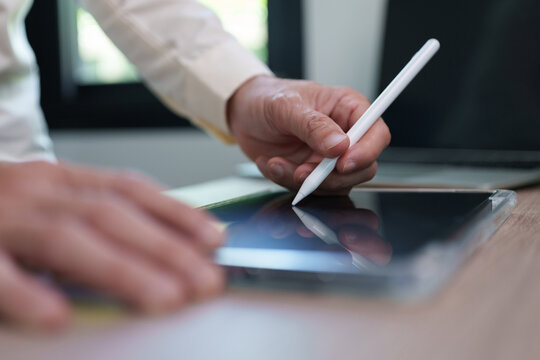 Close-up of a person using a stylus on a blank tablet screen at a desk, showing digital writing, creative workflow, business technology