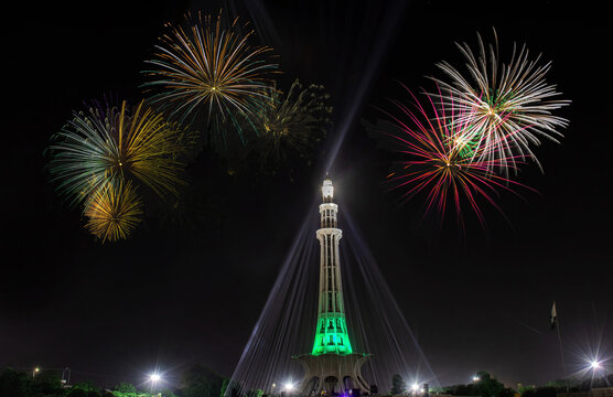 View of the illuminated Minar-e-Pakistan monument at night with vibrant fireworks displays in the sky above Lahore, Punjab, Pakistan.