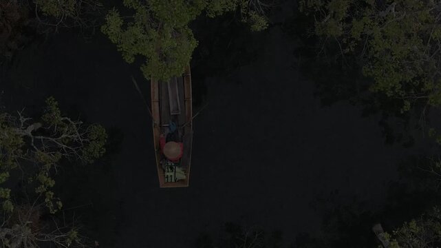 Aerial drone view of a fisherman rowing across Tuyen Lam Lake at sunrise near Suoi Tia in Xuan Huong, Da Lat, Vietnam, surrounded by peaceful pine forests.