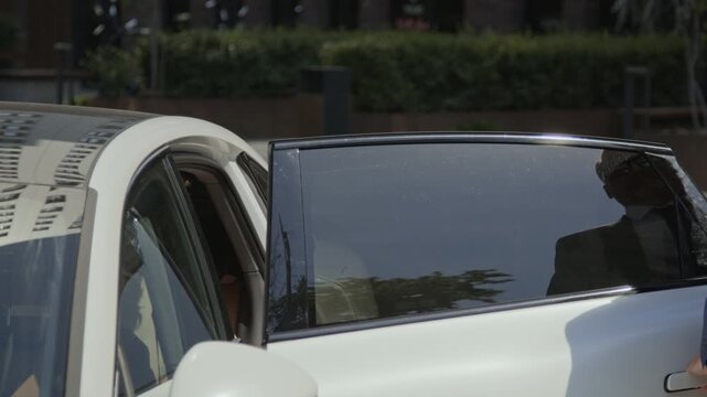 Middle-aged chauffeur opening electric car door for young adult Caucasian male passenger and getting into driver seat. Video is suitable for executive transport and ride-sharing promos