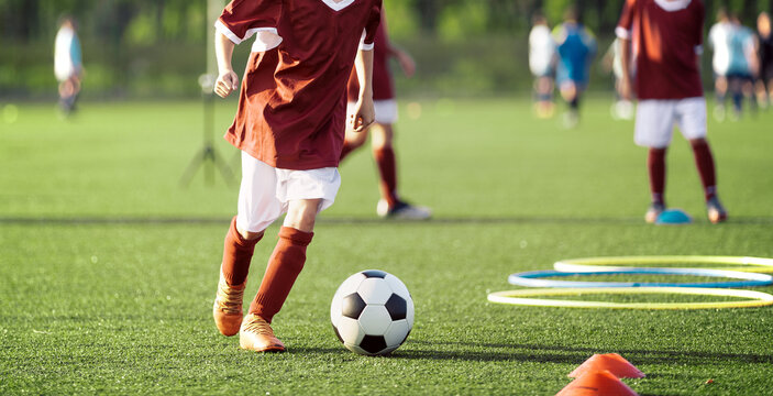 Young Football Player Dribbling Soccer Ball Near Training Hoops - Youth Agility Obstacle Course Practice on Sunny Pitch
