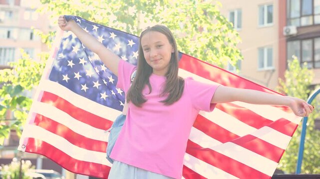 Happy teenage girl with backpack holding an American flag, student exchange program and studying abroad concept