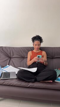 Young female student highlighting notes and getting distracted by her smartphone