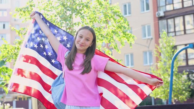 Happy teenage girl with backpack holding an American flag, student exchange program and studying abroad concept