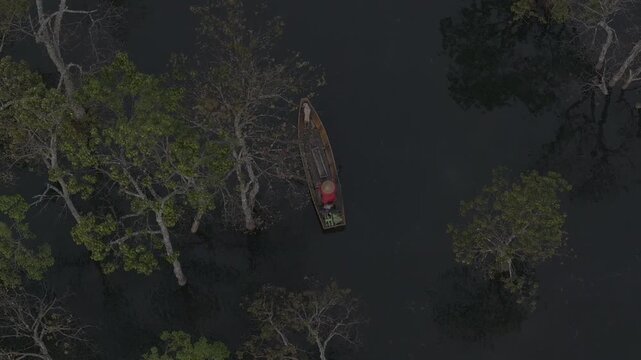 Aerial drone view of a fisherman rowing across Tuyen Lam Lake at sunrise near Suoi Tia in Xuan Huong, Da Lat, Vietnam, surrounded by peaceful pine forests.