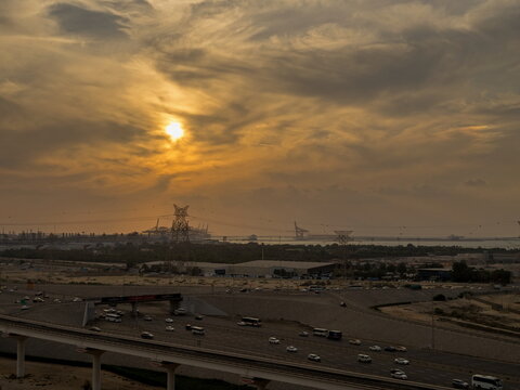 View of a multi-lane highway with vehicles driving under power lines during a golden sunset in Ras Al Khaimah, United Arab Emirates.