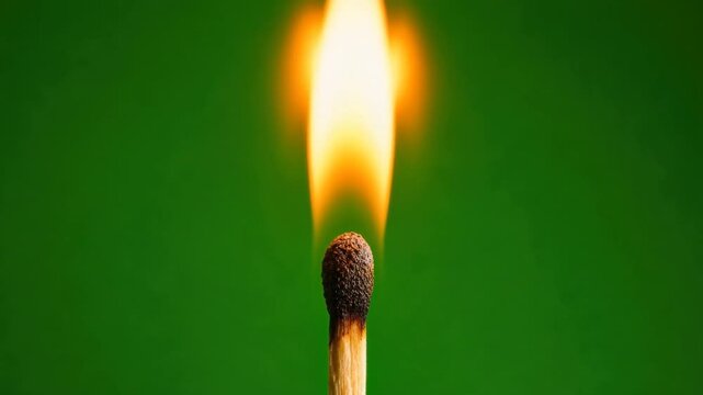 Close up of burning matchstick flame with bright orange fire and green background