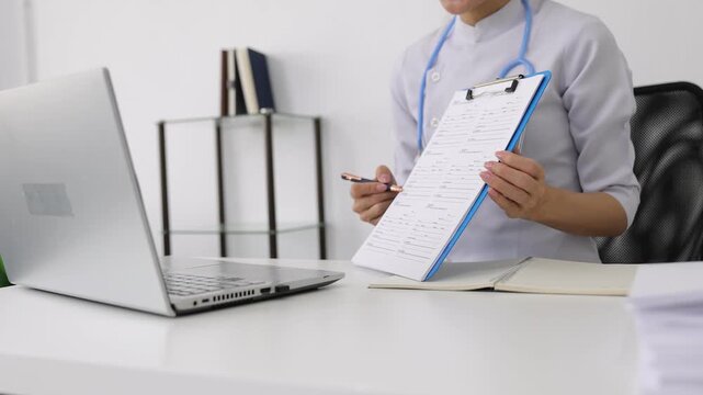 Asian female doctor explaining medical results online. Young Asian female doctor having a video call with a patient. She is showing a medical form on a clipboard and explaining the results.