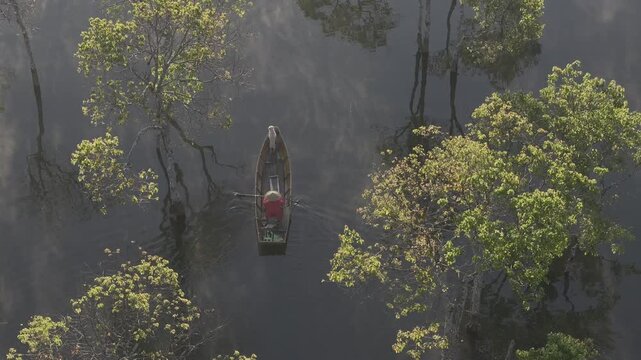 Aerial drone view of a fisherman rowing across Tuyen Lam Lake at sunrise near Suoi Tia in Xuan Huong, Da Lat, Vietnam, surrounded by peaceful pine forests.