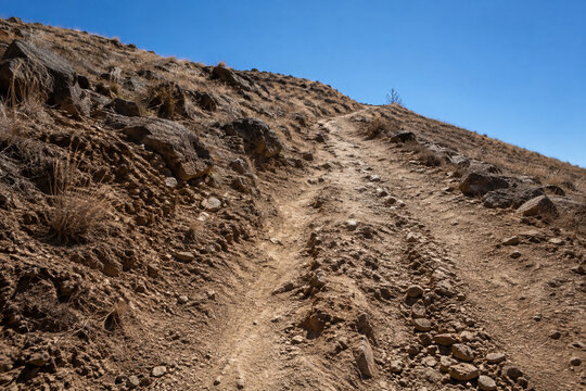 Steep unpaved trail on dry rocky hillside with ruts and exposed roots, arduous hiking path concept