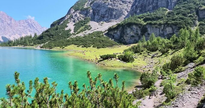 Moving real time view from an alpine trail revealing turquoise Seebensee with forest slopes and rugged mountains in Tyrol Austria.