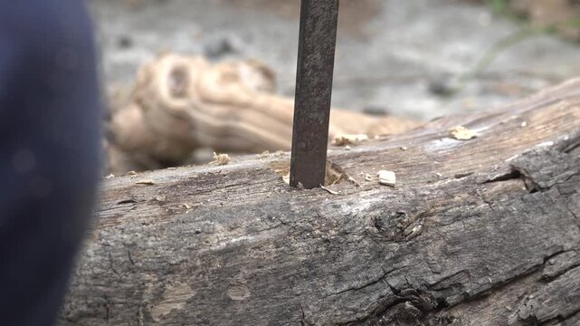 Over-the-shoulder angle of an artisan using a hand chisel to carve and shape a square recess in solid timber.

