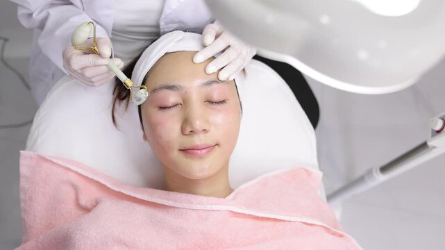 Professional aesthetician giving facial massage with jade roller.