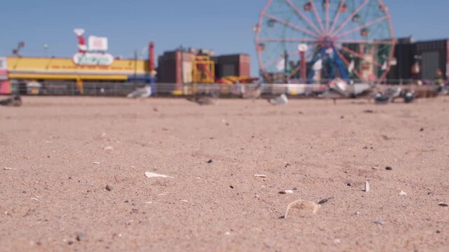 Coney Island sandy beach in Brooklyn, New York, United States. Boardwalk near retro luna park. Ferris wheel in american amusement park on ocean coast. Waterfront summer holiday promenade in NYC, USA.