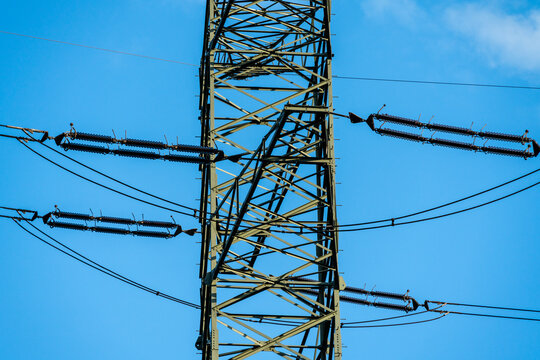 View of a high-voltage power transmission tower with metal lattice structure, electrical insulators, and power lines against blue sky in Dabrowa Gornicza, Silesian Voivodeship, Poland.
