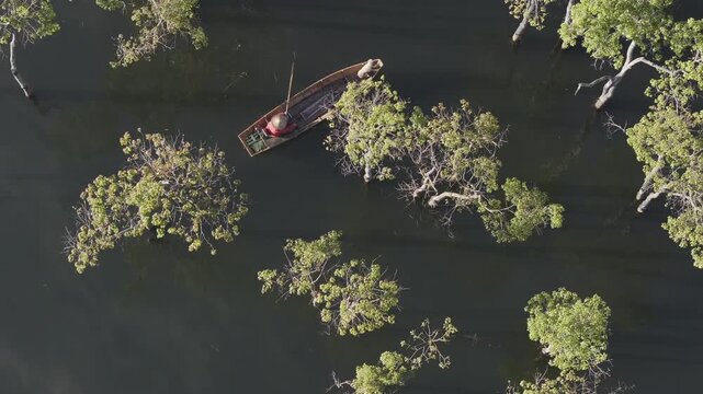Aerial drone view of a fisherman rowing across Tuyen Lam Lake at sunrise near Suoi Tia in Xuan Huong, Da Lat, Vietnam, surrounded by peaceful pine forests.