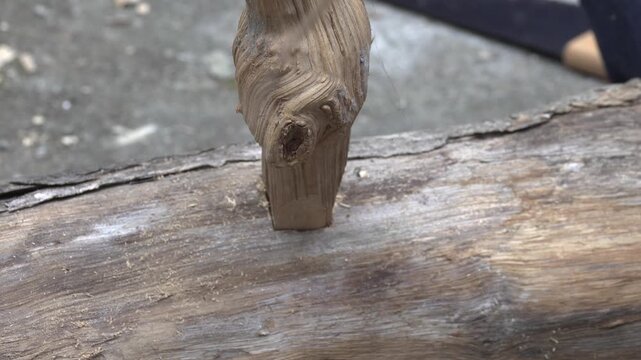 Carpenter inserts a shaped wooden tenon peg into a carved square mortise hole on a rustic log to test joint fitting accuracy.
