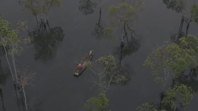 Aerial drone view of a fisherman rowing across Tuyen Lam Lake at sunrise near Suoi Tia in Xuan Huong, Da Lat, Vietnam, surrounded by peaceful pine forests.