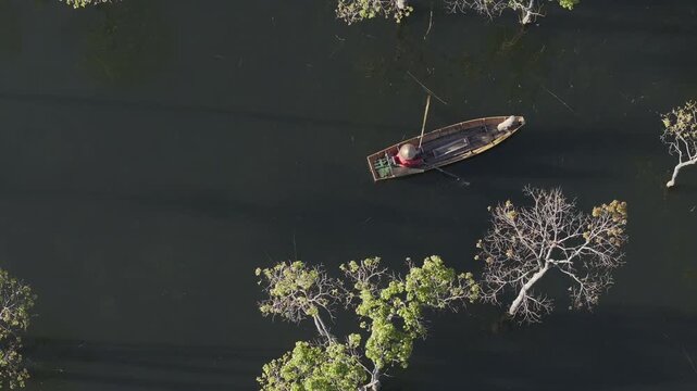Aerial drone view of a fisherman rowing across Tuyen Lam Lake at sunrise near Suoi Tia in Xuan Huong, Da Lat, Vietnam, surrounded by peaceful pine forests.