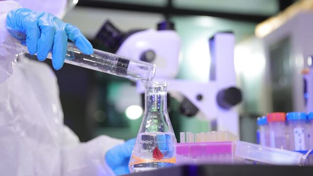Scientist wearing protective gear pouring liquid in a laboratory research.