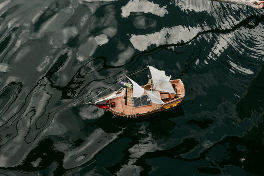 View of a small toy sailing ship floating on dark rippling water with sky reflections in Copenhagen, Denmark.