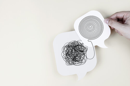 Hand holding speech bubble paper cut with messy tangle line untangled into organized spiral. Concept of mental health, therapy, problem solving, and clarifying thoughts.