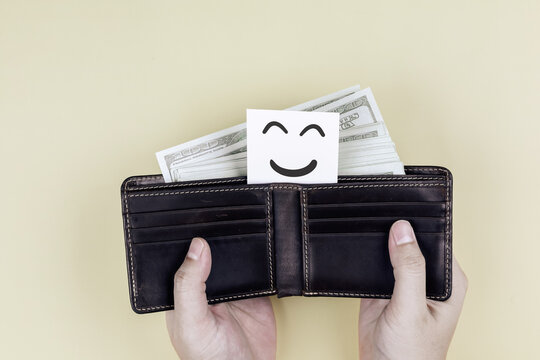 Hands opening leather wallet full of cash with happy smile face card. Concept of financial freedom, wealth happiness, and money savings success.
