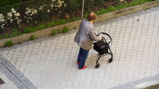 Abuela con andador caminador paseando coja movilidad en calle fuerza de voluntad y esfuerzo dependiente tercera edad paseo por acera