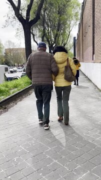 Paseo matrimonio pareja del brazo de espaldas andando por acera calle dos adultos paseando con abrigo en oto&ntilde;o invierno casados tercera edad